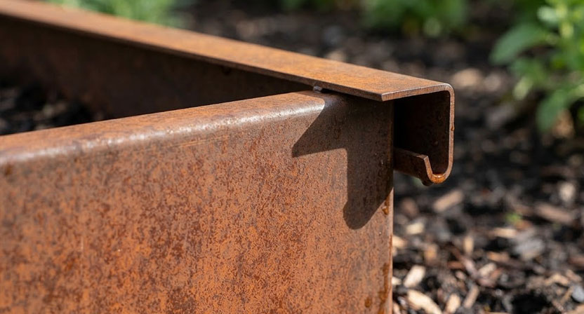 Rand eines Cortenstahl-Hochbeets von der Seite: die Metallkante ist nach außen und dann nach unten gefalzt und bildet eine überhängende Lippe